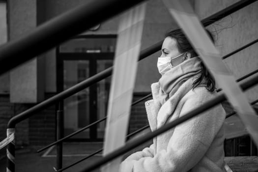 Photo of a girl in a mask. Sitting on the street with danger warning tapes. isolated Covid-19 pandemic.