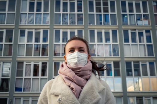 Shot of a girl in wearing face mask for protection, on the street. Against the background of a residential building with windows. lockdown Covid-19 pandemic.