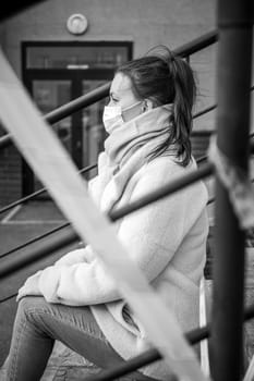 Photo of a girl in a mask. Sitting on the street with danger warning tapes. isolated Covid-19 pandemic.