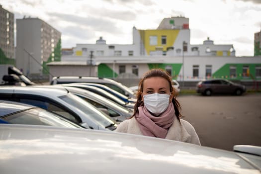 picture of a girl in a mask, on the street. Against the background of parked cars. isolated Covid-19 pandemic.