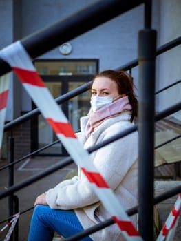 Photo of a girl in a mask. Sitting on the street with danger warning tapes. isolated Covid-19 pandemic.