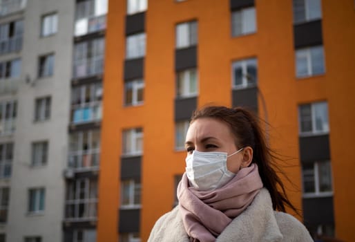 Shot of a girl in wearing face mask for protection, on the street. Against the background of a residential building with windows. lockdown Covid-19 pandemic.