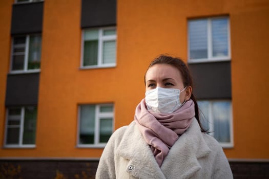 Shot of a girl in wearing face mask for protection, on the street. Against the background of a residential building with windows. lockdown Covid-19 pandemic.