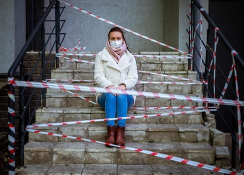 Photo of a girl in a mask. Sitting on the street with danger warning tapes. isolated Covid-19 pandemic.