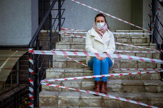 Photo of a girl in a mask. Sitting on the street with danger warning tapes. isolated Covid-19 pandemic.