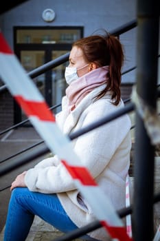 Photo of a girl in a mask. Sitting on the street with danger warning tapes. isolated Covid-19 pandemic.