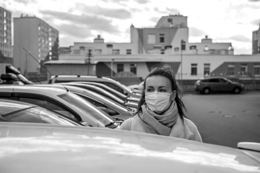 picture of a girl in a mask, on the street. Against the background of parked cars. isolated Covid-19 pandemic.