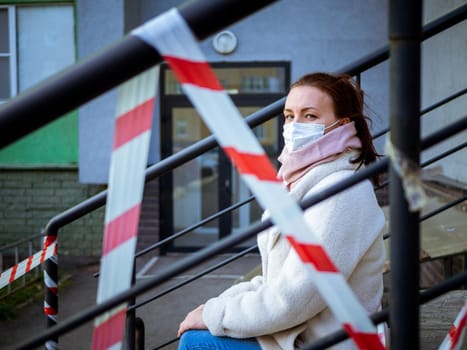 Photo of a girl in a mask. Sitting on the street with danger warning tapes. isolated Covid-19 pandemic.