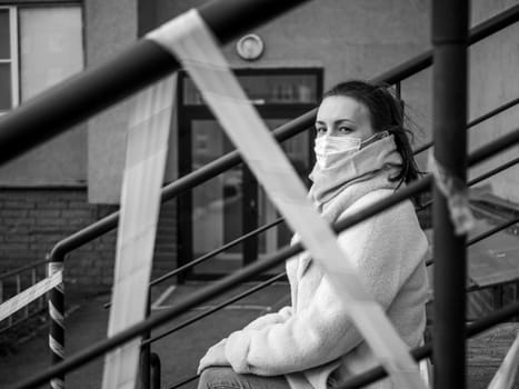 Photo of a girl in a mask. Sitting on the street with danger warning tapes. isolated Covid-19 pandemic.