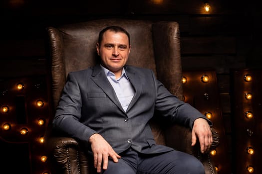 handsome businessman in a suit looks at the camera on a leather chair. isolated on a black background