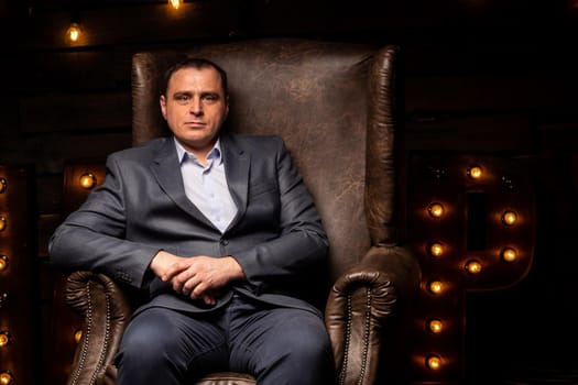 handsome businessman in a suit looks at the camera on a leather chair. isolated on a black background