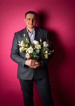 handsome businessman in a suit looks at the camera with a bouquet of flowers. isolated on a pink background