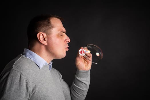handsome man in a suit is blowing soap bubbles. isolated on a black background