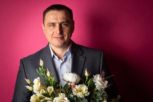 handsome businessman in a suit looks at the camera with a bouquet of flowers. isolated on a pink background