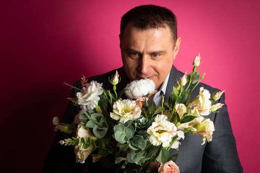 handsome businessman in a suit looks at the camera with a bouquet of flowers. isolated on a pink background