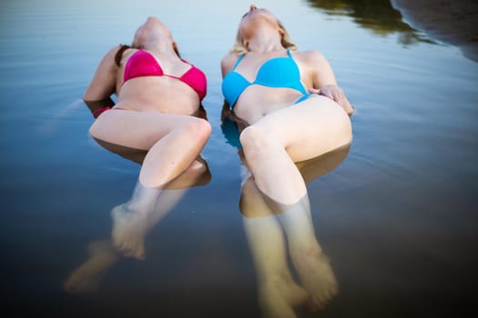 Front view of two young women with beautiful bodies in bikinis. Blue and pink swimsuit in the water.