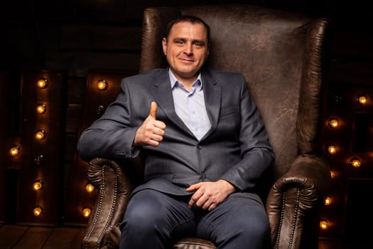 handsome businessman in a suit looks at the camera on a leather chair. isolated on a black background