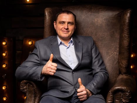 handsome businessman in a suit looks at the camera on a leather chair. isolated on a black background