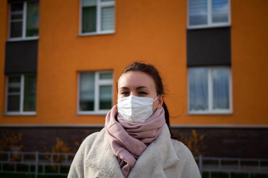 Shot of a girl in wearing face mask for protection, on the street. Against the background of a residential building with windows. lockdown Covid-19 pandemic.