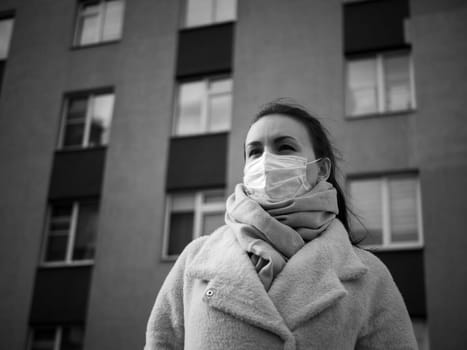 Shot of a girl in wearing face mask for protection, on the street. Against the background of a residential building with windows. lockdown Covid-19 pandemic.