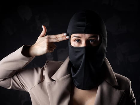 Portrait of a girl in a black balaclava and beige coat. Shot in the studio on a dark background.