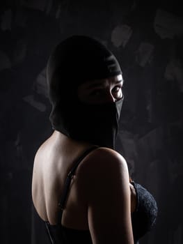 Portrait of a girl in a black balaclava and a black bra. Shot in the studio on a dark background.