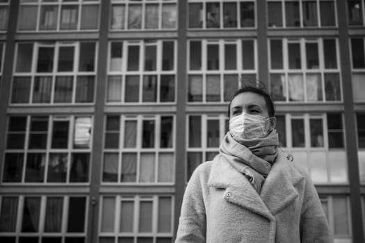 Shot of a girl in wearing face mask for protection, on the street. Against the background of a residential building with windows. lockdown Covid-19 pandemic.