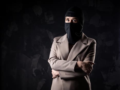 Portrait of a girl in a black balaclava and beige coat. Shot in the studio on a dark background.