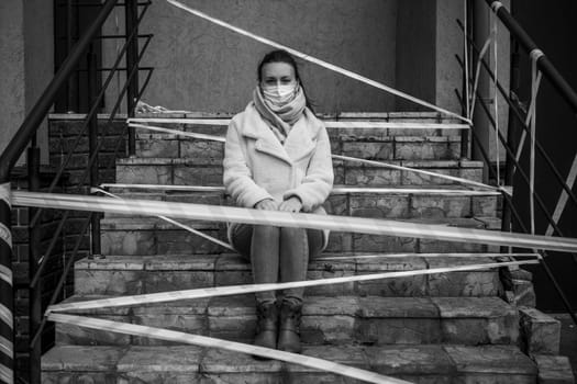 Photo of a girl in a mask. Sitting on the street with danger warning tapes. isolated Covid-19 pandemic.