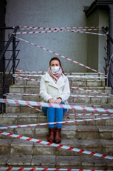 Photo of a girl in a mask. Sitting on the street with danger warning tapes. isolated Covid-19 pandemic.