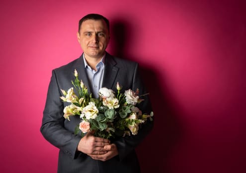 handsome businessman in a suit looks at the camera with a bouquet of flowers. isolated on a pink background