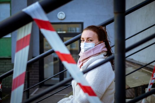 Photo of a girl in a mask. Sitting on the street with danger warning tapes. isolated Covid-19 pandemic.