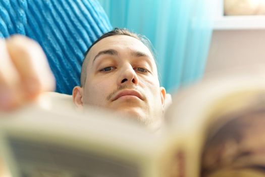 Leisure, education, literature and home concept close up of man lying on couch and reading book at home. Selective focus