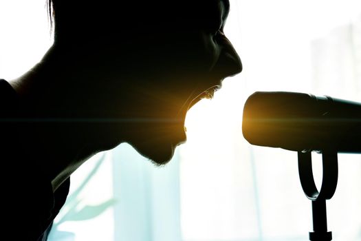 One person sings into the microphone for a copy space. Silhouette of a male singer, selective focus