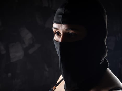 Portrait of a girl in a black balaclava and a black bra. Shot in the studio on a dark background.