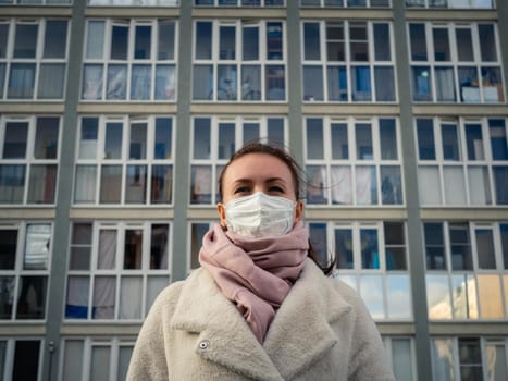 Shot of a girl in wearing face mask for protection, on the street. Against the background of a residential building with windows. lockdown Covid-19 pandemic.