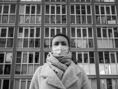 Shot of a girl in wearing face mask for protection, on the street. Against the background of a residential building with windows. lockdown Covid-19 pandemic.