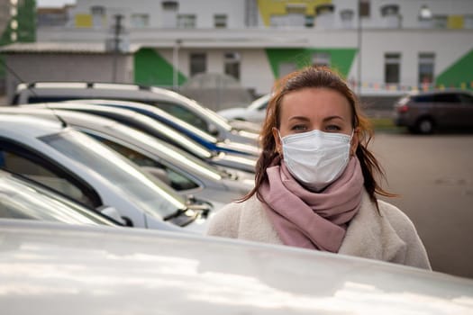 picture of a girl in a mask, on the street. Against the background of parked cars. isolated Covid-19 pandemic.