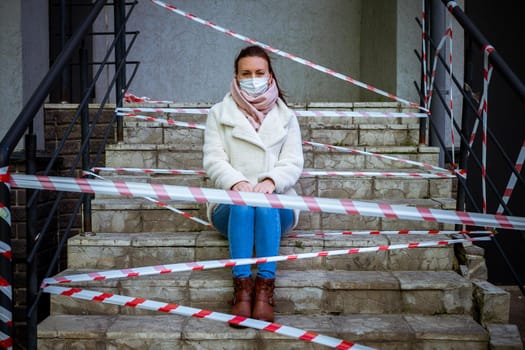 Photo of a girl in a mask. Sitting on the street with danger warning tapes. isolated Covid-19 pandemic.