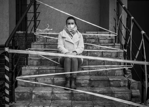 Photo of a girl in a mask. Sitting on the street with danger warning tapes. isolated Covid-19 pandemic.