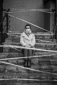 Photo of a girl in a mask. Sitting on the street with danger warning tapes. isolated Covid-19 pandemic.