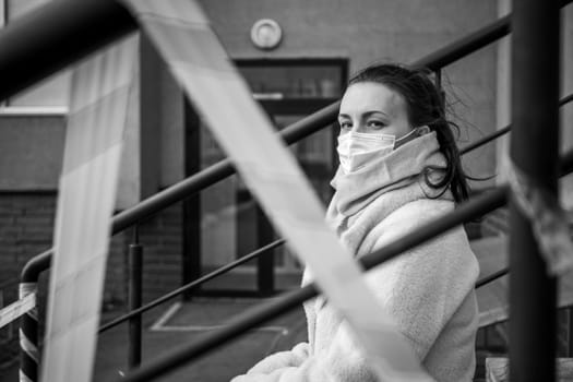 Photo of a girl in a mask. Sitting on the street with danger warning tapes. isolated Covid-19 pandemic.