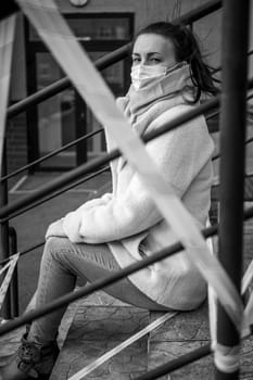 Photo of a girl in a mask. Sitting on the street with danger warning tapes. isolated Covid-19 pandemic.