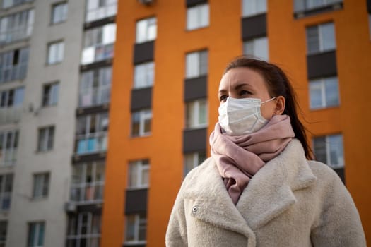 Shot of a girl in wearing face mask for protection, on the street. Against the background of a residential building with windows. lockdown Covid-19 pandemic.