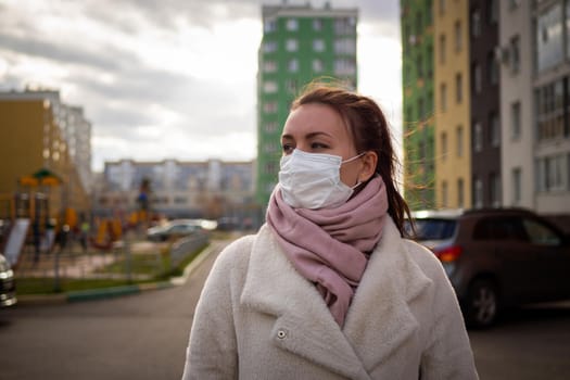 Shot of a girl in wearing face mask for protection, on the street. Against the background of a residential building with windows. lockdown Covid-19 pandemic.