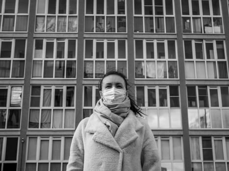 Shot of a girl in wearing face mask for protection, on the street. Against the background of a residential building with windows. lockdown Covid-19 pandemic.