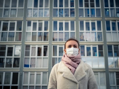 Shot of a girl in wearing face mask for protection, on the street. Against the background of a residential building with windows. lockdown Covid-19 pandemic.