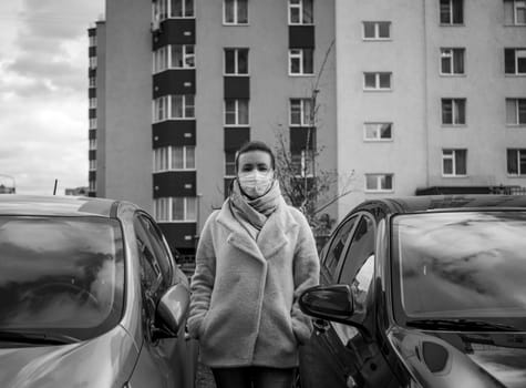 picture of a girl in a mask, on the street. Against the background of parked cars. isolated Covid-19 pandemic.