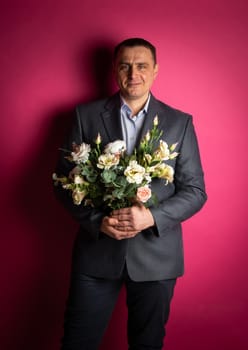 handsome businessman in a suit looks at the camera with a bouquet of flowers. isolated on a pink background