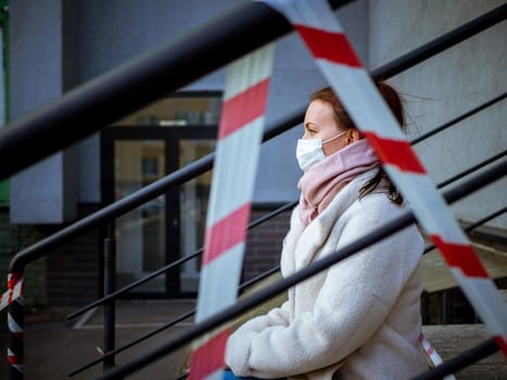 Photo of a girl in a mask. Sitting on the street with danger warning tapes. isolated Covid-19 pandemic.